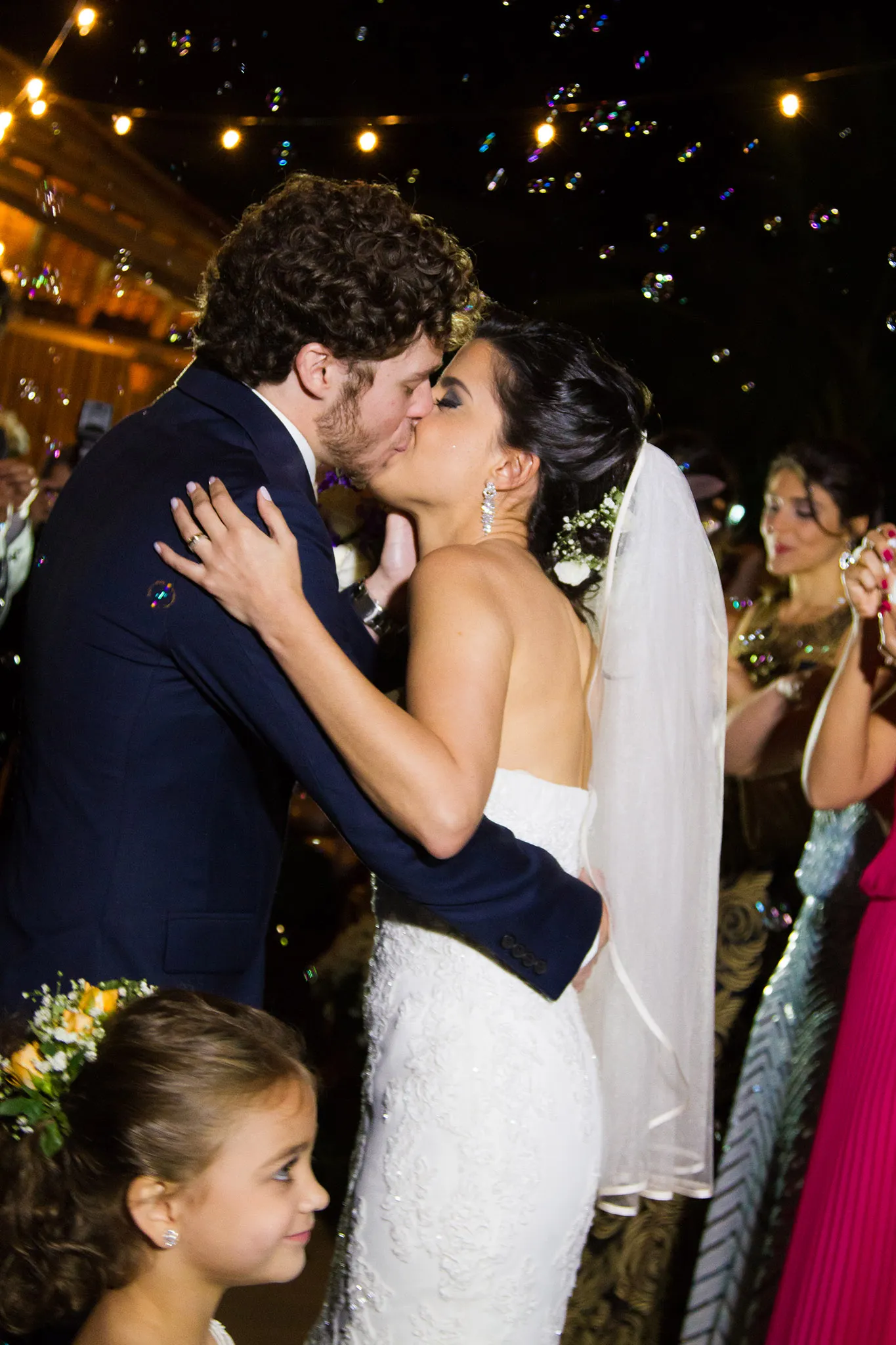 Os noivos se beijando no meio da festa, com uma menina em primeiro plano
