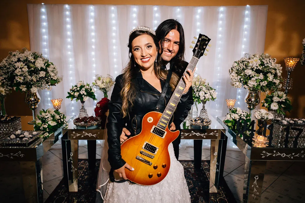 Juliana segurando uma guitarra e rindo com Rafael diante da mesa do bolo