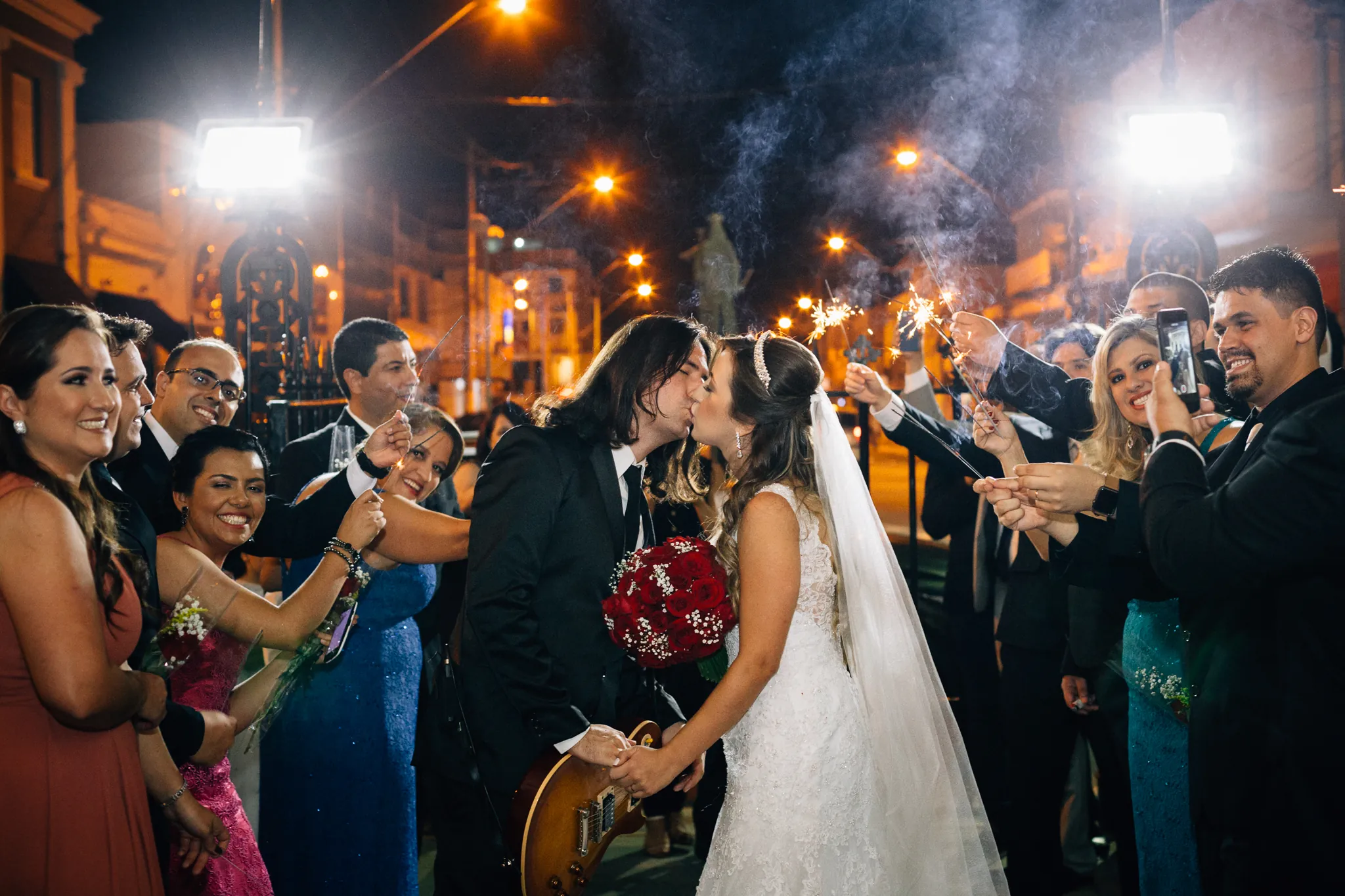 Os noivos se beijando na saída, à noite, entre os convidados com velas faiscantes